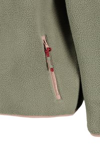 Chaqueta de forro polar verde con un bolsillo de cremallera rosa que presenta un tirador de cremallera rojo en el lado inferior.