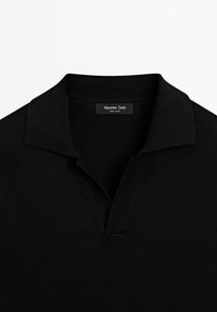 Sort polo-shirt med blød tekstur, der har en klassisk krave og en halv knaplukning. Mærket lyder "Massimo Dutti."