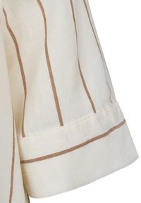 Cremefarbener Leinenstoff mit braunen Verticalstreifen. Besitzt einen Ärmel mit einem sauber genähten Saum. Weiche Textur und lockere Passform.