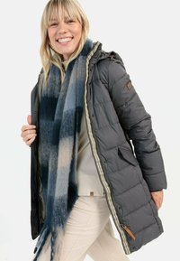 Grijze pufferjack met een capuchon, voorzien van een gestreepte rits, patchdetail en zijzakken. Gecombineerd met een blauw en grijs geruite sjaal.