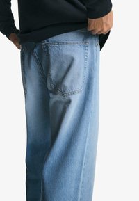 Helleblaue Denim-Jeans mit entspannter Passform, die über zwei Gesäßtaschen und dezente Nähte verfügt. Getragen mit einem schwarzen Oberteil.