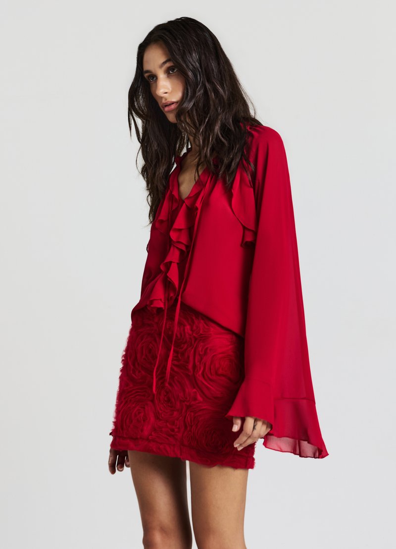 Blouse rouge avec un col froncé et des manches évasées, associée à une jupe rouge ornée d'un motif de roses. Les deux vêtements ont une texture lisse.