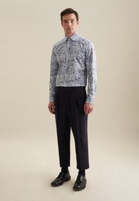 Knoopshirt in lichtblauw met een bloemmotief; gecombineerd met donker marineblauwe broeken en zwarte nette schoenen. Glad materiaal, getailleerde pasvorm.