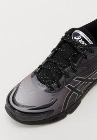 Svart och grå atletisk sko med en texturerad yta, snörning och Asics-logotyp på tungan. Har mönstrade detaljer.