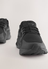 Czarne buty sportowe z siateczkową cholewką, teksturowanymi akcentami oraz amortyzowaną podeszwą z trwałym wzorem bieżnika.