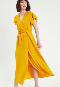 Maxi wrap dress in bright yellow, featuring flutter sleeves, a belted waist, and a side slit for ease of movement. Textured fabric.