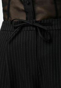 Pantalon noir à fines rayures avec une texture tissée, doté d'une taille nouée. Le tissu présente des rayures subtiles bleues et blanches.