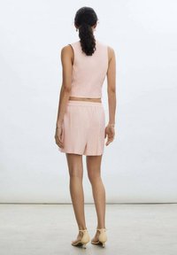 Haut court à côtes rose clair avec un short assorti, doté d'une taille élastique. Le mannequin porte des talons beiges clairs. L'arrière-plan est neutre.