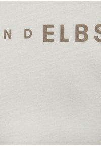 Ein hellgraufarbenes Gewebe zeigt großen, fetten Text "ELBS" in Braun. Die Textur wirkt glatt und hat einen leichten Glanz.