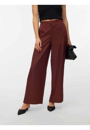 Donna con pantaloni ampi color bordeaux, top nero senza maniche, ballerine nere appuntite e una pochette nera in mano.