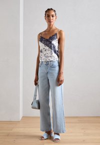 Camiseta de encaje floral en blanco y marino; jeans de pierna ancha en azul claro; sandalias de tacón en azul pálido; llevando un bolso en azul claro.