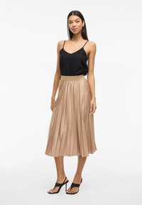 Čierny textúrovaný top bez rukávov v kombinácii s plisovanou béžovou midi sukňou, ktorá má hladký pás a čierne sandále na vysokom podpätku. Jednoduchý a elegantný dizajn.