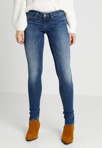 Smal blå denimjeans med en urblekt finish, femficksdesign och silverdetaljer, tillsammans med orange ankelstövlar.