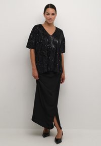 Black sequin top with a V-neck and short sleeves paired with a black maxi skirt featuring a side slit. Black pointed heels complete the outfit.