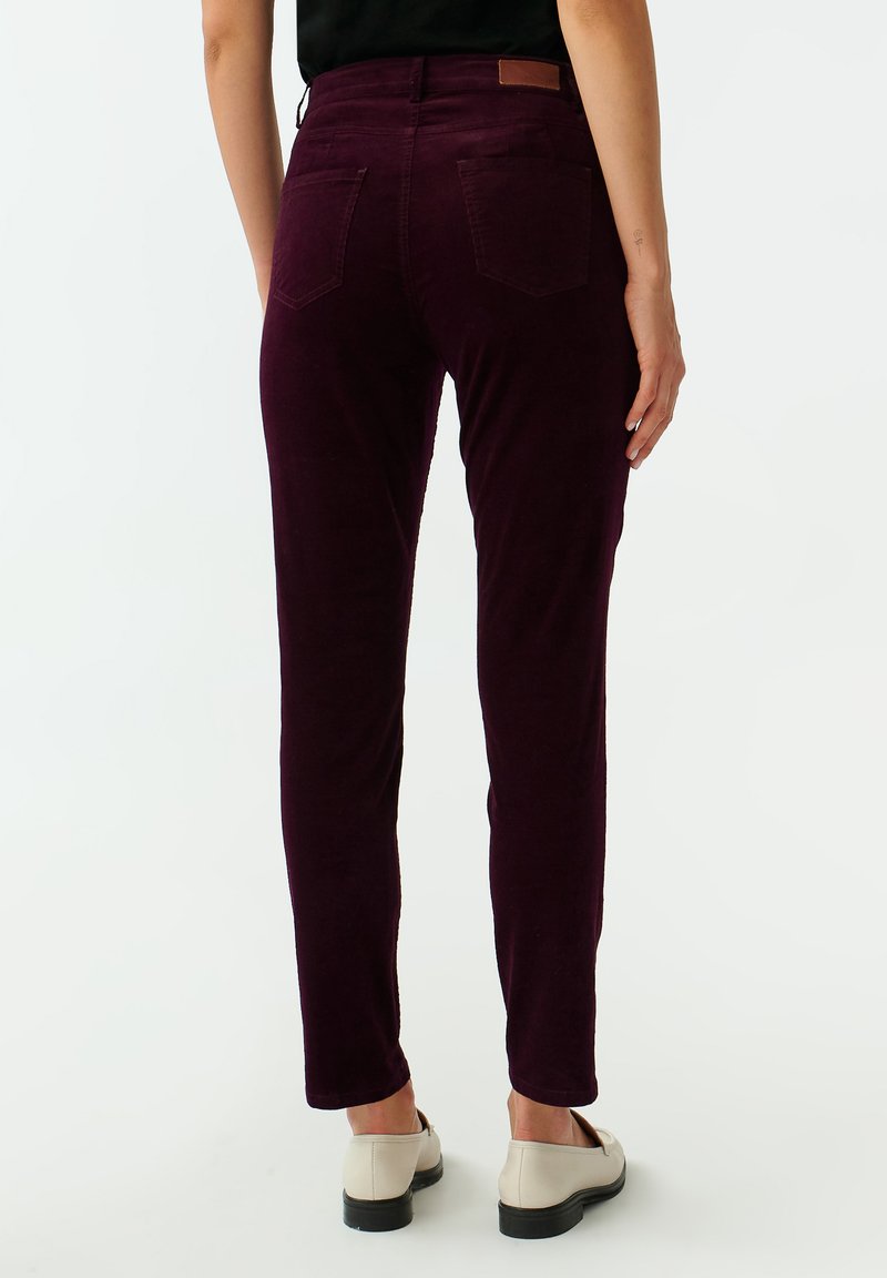 Bordowe spodnie z sztruksu o slim fit, z dwiema tylnymi kieszeniami i brązową skórzaną łatą przy pasie. Gładka faktura i dopasowane nogawki.