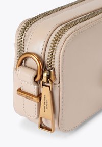 Sac bandoulière en cuir beige avec quincaillerie dorée, fermeture à double fermeture éclair et étiquette de marque. Présente une finition lisse et texturée.