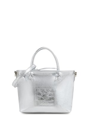 Bolso tote metálico plateado con dos asas, bandolera ajustable, parche frontal con marca en relieve y detalles anudados cerca de las asas.