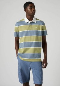 Polo con righe orizzontali verdi, blu e bianche, con colletto bianco e logo ricamato. Indossato con pantaloni cargo blu chiaro.