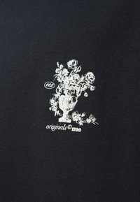 Μαύρο ύφασμα με λευκό σχέδιο ανθοφόρου βάζου και κείμενο "102 originals ©1990," που τονίζει στοιχεία vintage αισθητικής.