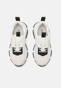 White sneakers with mesh, suede, and rubber material. Features black accents, white laces, and a looped pull tab on the heel. Chunky sole design.