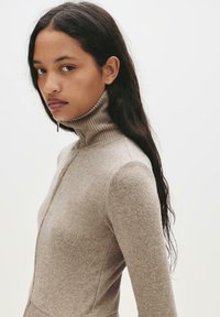 Beige ribbet turtle neck sweater lavet af blødt materiale, med et tætsiddende design og lange ærmer, samt en kvart lynlås foran.