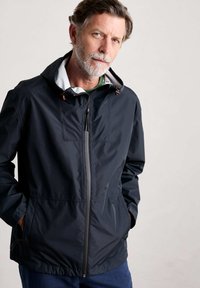 Marinblå vattentät jacka med frontdragkedja, vit huva med foder och justerbara dragsnören. Har sidofickor och en avslappnad passform.