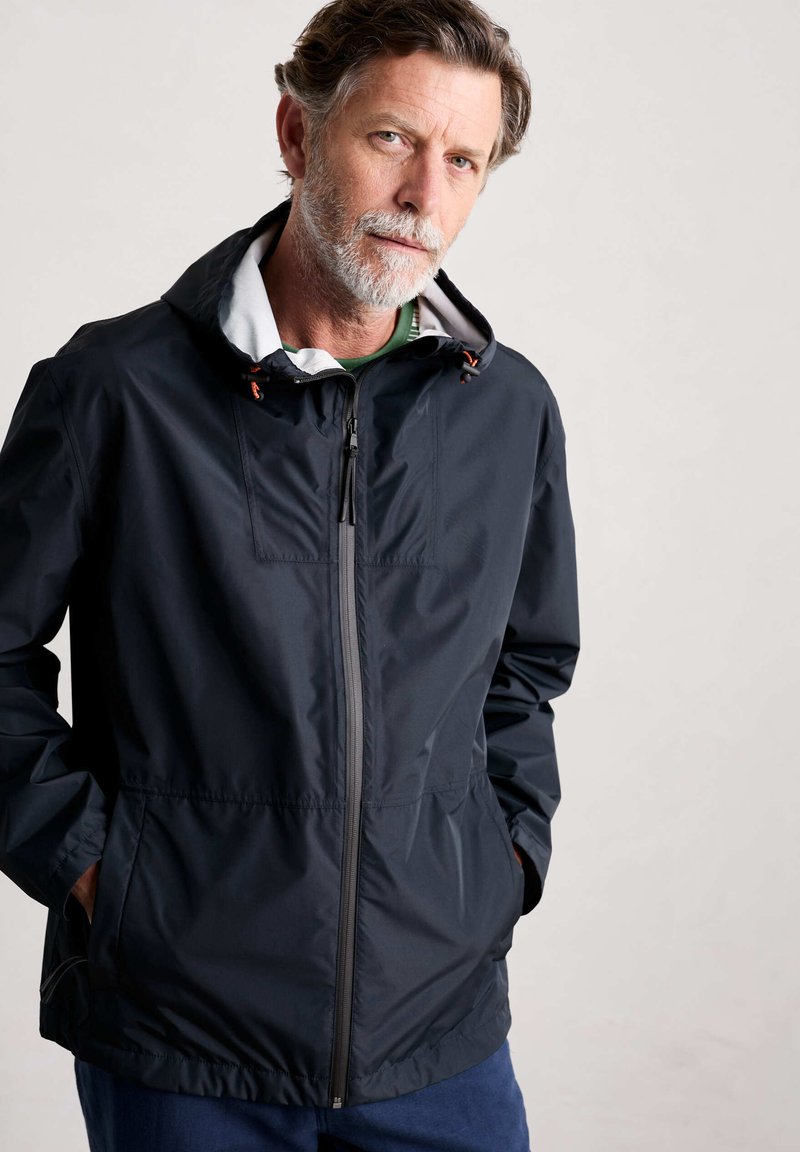 Marinblå vattentät jacka med frontdragkedja, vit huva med foder och justerbara dragsnören. Har sidofickor och en avslappnad passform.