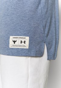 Camiseta de algodón azul claro con mangas cortas y aberturas laterales. Presenta una etiqueta blanca con gráficos negros cerca del dobladillo.