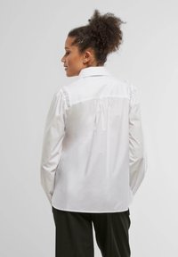 Hvit skjorte med knapper og strukturert krage, puffete ermer og rynkede detaljer på baksiden, laget av glatt, lett stoff.