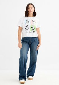 Camiseta corta blanca con un gráfico de Mickey Mouse en cuatro colores en la parte frontal, combinada con jeans azules de tiro alto y acampanados.