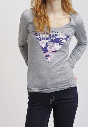 T-shirt gris à manches longues avec un col dégagé, présentant un design graphique triangulaire noir et blanc sur le devant. Tissu doux et ajusté.