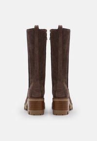 Bottes montant jusqu'aux genoux en suède marron avec un talon en bois épais et une fermeture éclair latérale. Surface texturée avec des panneaux noirs verticaux pour le contraste.