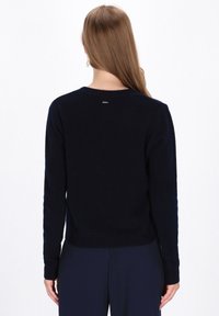 Maglione a maglia blu navy con collo rotondo classico, polsini e fondo a costine. Presenta un piccolo logo vicino al collo. Texture morbida.
