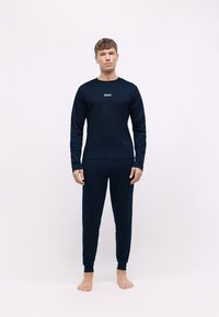 Camisa de manga larga azul marino y pantalones a juego, confeccionados con tela suave, que presentan un pequeño logo blanco en el pecho, con puños acanalados en las muñecas y tobillos.