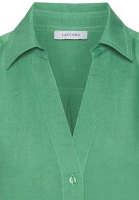 Green linen blouse with a collar, V-neckline, and a button closure. Features a textured fabric and straight seams for a clean finish.