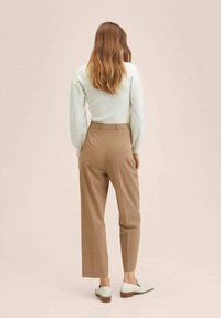 Haut à manches longues côtelé crème associé à un pantalon marron taille haute et des mocassins verts menthe. Tissu lisse avec une coupe cintrée ; design minimaliste.