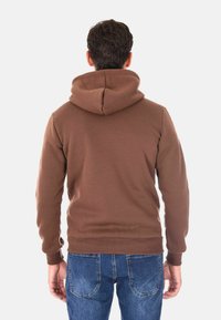 Felpa con cappuccio marrone dal texture morbida, con polsini e orlo a costine; indossata con jeans in denim blu, vista da dietro.