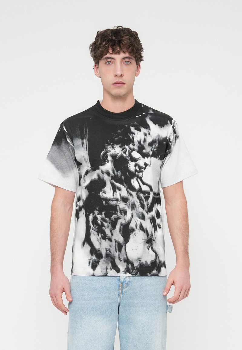 Κοντομάνικη μπλούζα από βαμβάκι, με ασπρόμαυρο αφηρημένο σχέδιο και έντονο γραφικό τύπωμα. Λαιμόκοψη στρόγγυλη και άνετη εφαρμογή.