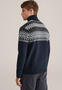 Pulover tricotat bleumarin cu guler înalt, având un model geometric alb și verde pe umeri, cu manșete și tiv cu dungi.