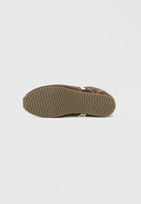 Hnědá nubuková podrážka s texturovanou gumovou podrážkou. Obsahuje vzor zoubkovaného profilu a bílé švy.