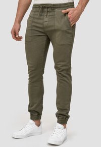 Pantalones de chándal en verde olivo, fabricados en algodón, con piernas ajustadas, cinturilla elástica con cordón y bolsillos frontales.