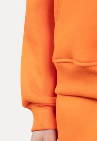 Sudadera naranja con puños y dobladillo de canalé, elaborada en algodón suave. Presenta un corte relajado y una textura suave.