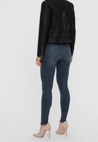 Jeans skinny blu scuro con vita alta, orlo sfrangiato e cuciture a contrasto. Abbinati a una giacca di pelle nera e tacchi beige.