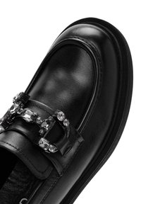 Zwarte leren instapper met een ronde neus, voorzien van een decoratieve gesp versierd met heldere rhinestones en een gladde, gestructureerde oppervlakte.