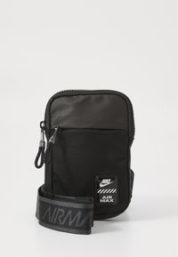 Geantă crossbody din nailon negru, cu suprafață texturată, închidere cu fermoar și curea ajustabilă, având imprimeu "AIR MAX" și logo-ul Nike.