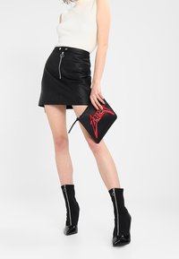 Czarna skórzana mini spódnica z zamkiem błyskawicznym z przodu, połączona z białym, żebrowanym topem na ramiączkach i czarnymi botkami z zamkiem do kostek. Nosi czarną kopertówkę z czerwonymi akcentami.