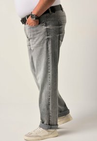 Jeans in denim grigio con una vestibilità rilassata, caratterizzati da una trama strappata, orli risvoltati e dettagli usurati. Abbinati a sneakers beige.