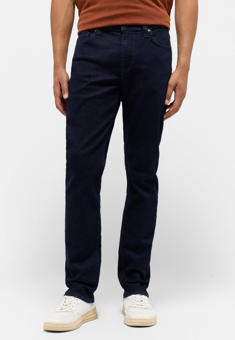 Granatowe dżinsy o slim fit, pięć kieszeni i subtelne przeszycia. Połączone z białymi trampkami dla swobodnego wyglądu.