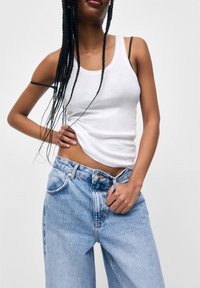 Top de tirantes blanco de algodón combinado con jeans de cintura alta azul claro. El top tiene tirantes estrechos y un diseño ceñido, que acentúa la cintura.