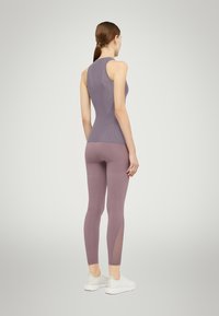 Top viola senza maniche con design testurizzato, abbinato a leggings viola chiaro con dettaglio in rete sul lato e scarpe sportive bianche.